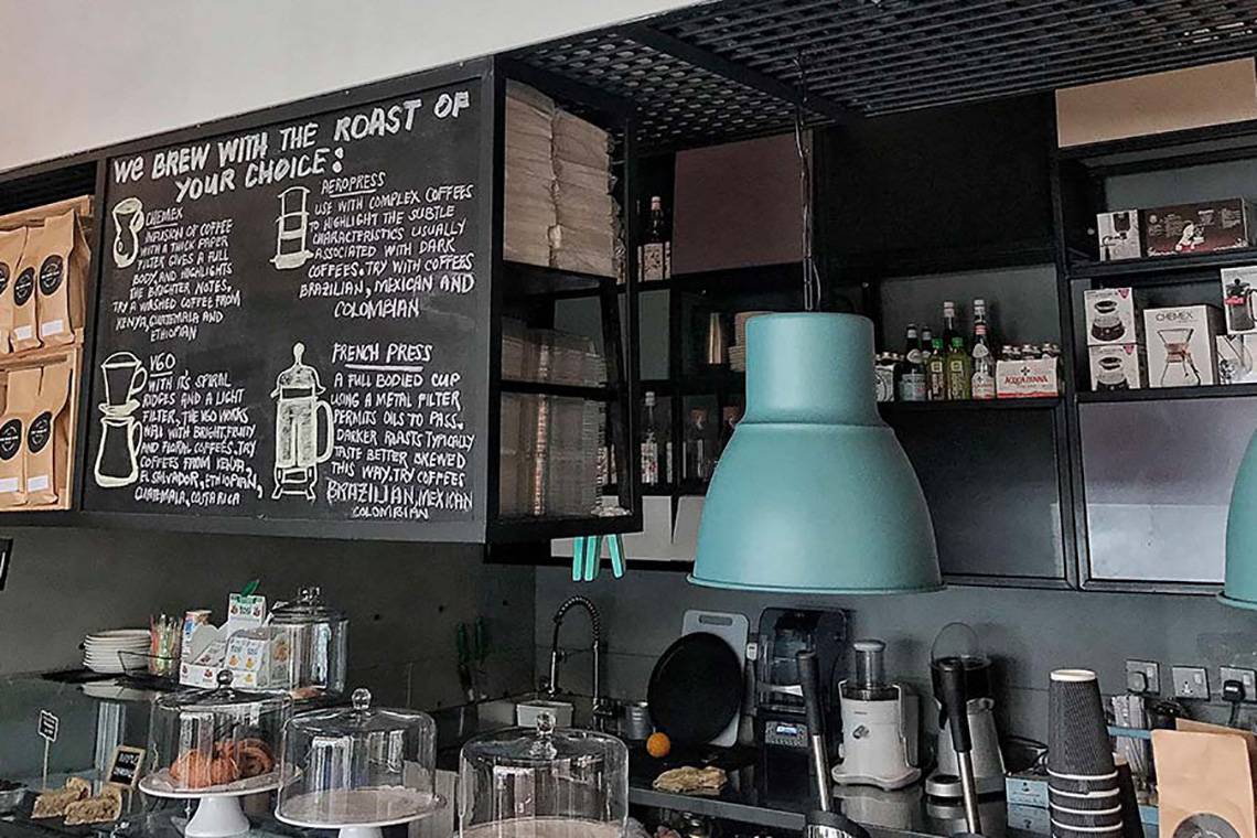 Inneneinrichtung des Jannah Hotels Resorts & Villas zeigt eine Bar mit einem schwarzen Wandboard und einer Tafel, die die Kaffeesorten beschreibt.