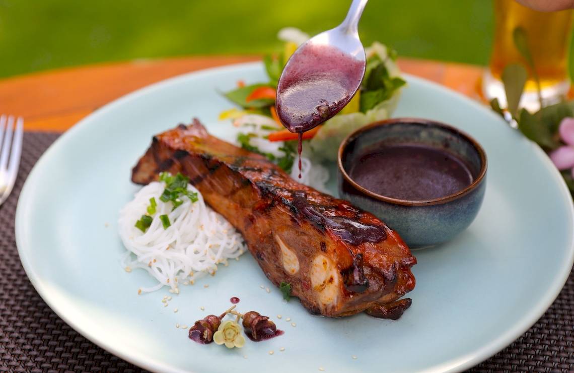 Gegrilltes Schweinefleisch auf einem Teller mit Sauce und Gemüse.