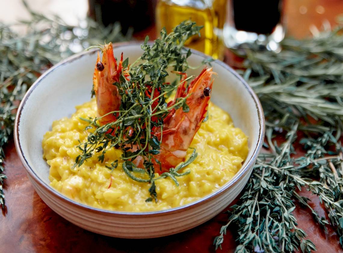 Eine Schüssel mit gelbem Risotto, das mit zwei gegrillten Garnelen und frischem Thymian garniert ist.
