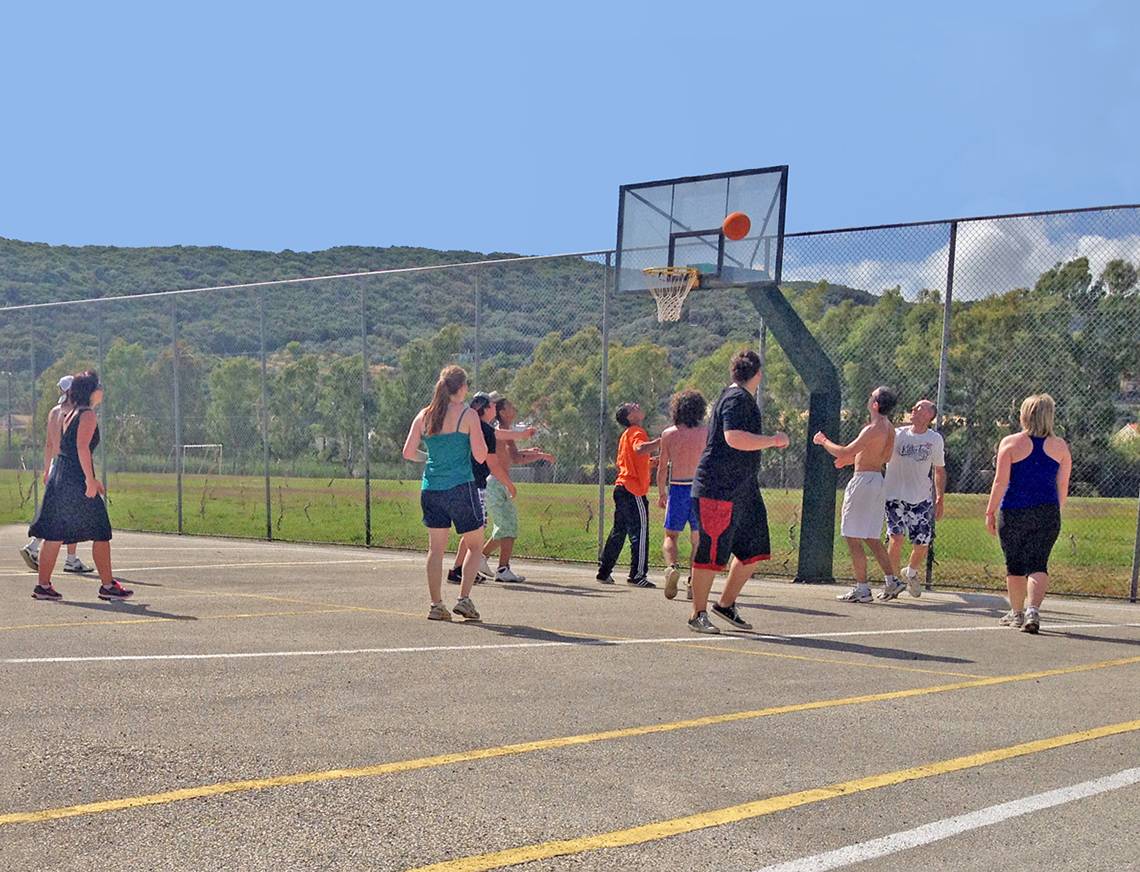 Mehrere Personen spielen Basketball auf einem Freiplatz, mit einem Bergpanorama im Hintergrund.