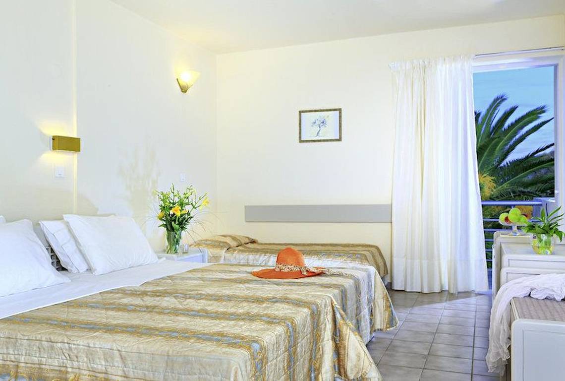 Schlafzimmer im Giannoulis Santa Marina Beach Hotel mit zwei Betten, Balkon und Blick auf Palmen.