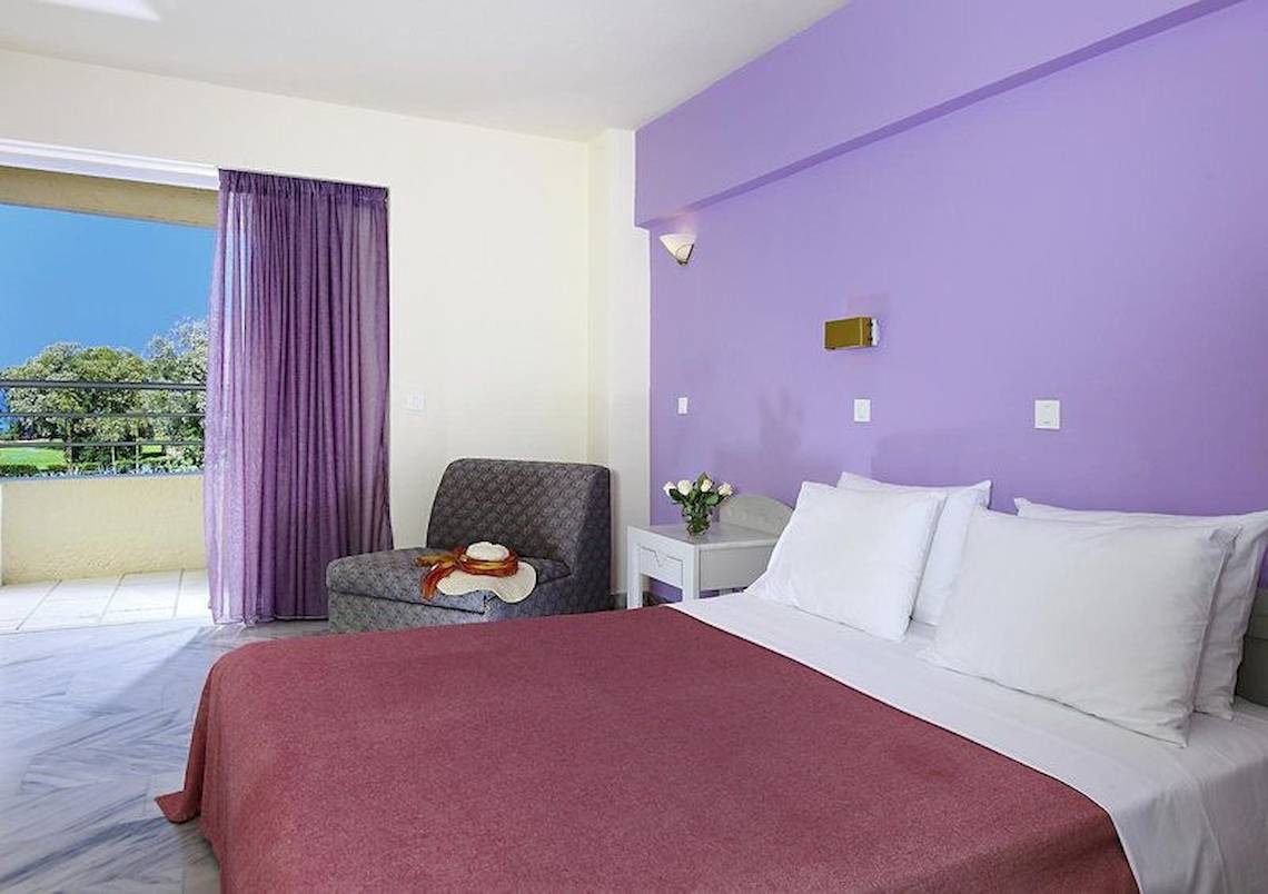 Schlafzimmer im Giannoulis Santa Marina Beach Hotel mit lila Wand, Bett, Kissen, und Balkon.