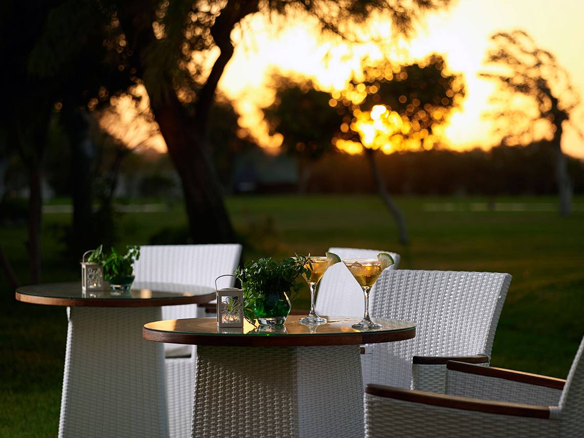 Sitzplätze im Freien am Mitsis Ramira Beach Hotel bei Sonnenuntergang mit Getränken auf dem Tisch.