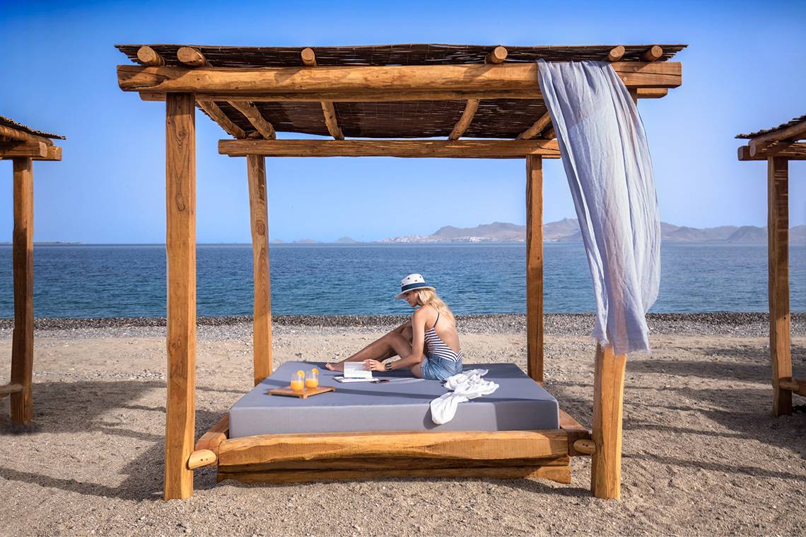 Frau liest Buch auf Strandbett am Meer des Mitsis Ramira Beach Hotels