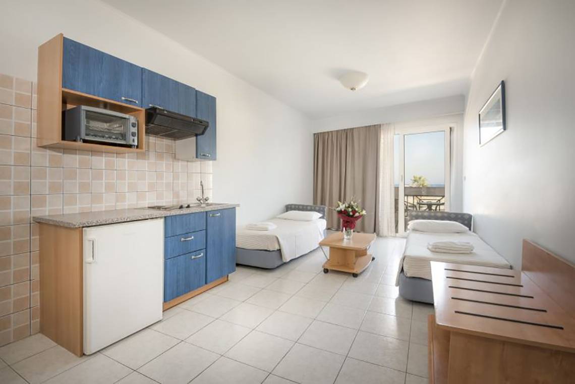 Innenansicht eines Zimmers im Kosta Palace City Hotel mit Küchenzeile, zwei Betten und Balkonzugang.