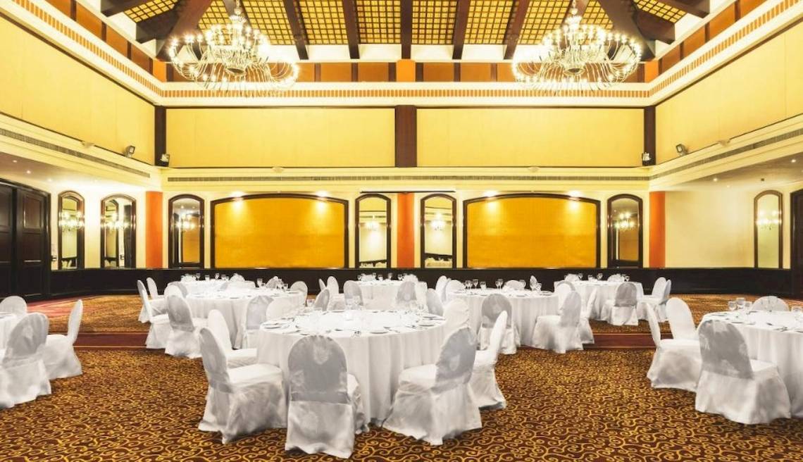 Bankettsaal im Le Meridien Ile Maurice mit weißen Tischen und Stühlen, goldenen Wänden und Kronleuchtern.