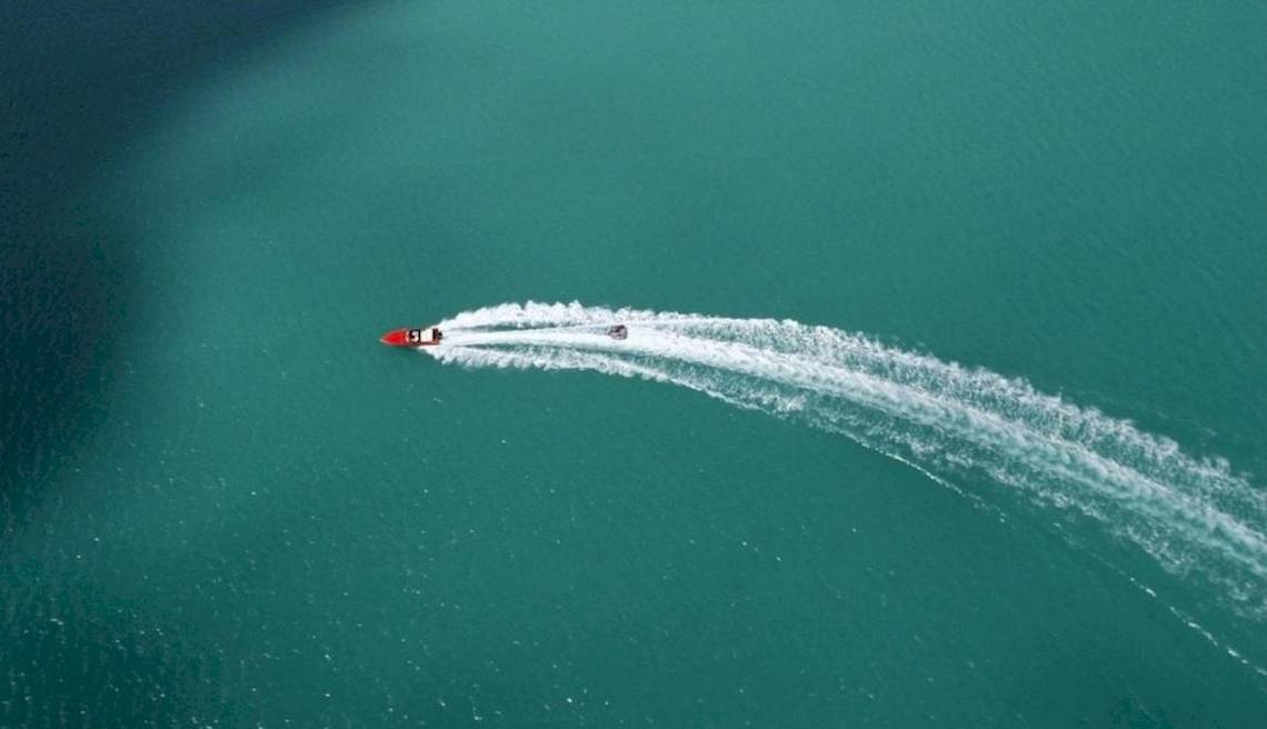 Ein rotes Boot fährt im Meer und hinterlässt eine weiße Spur.