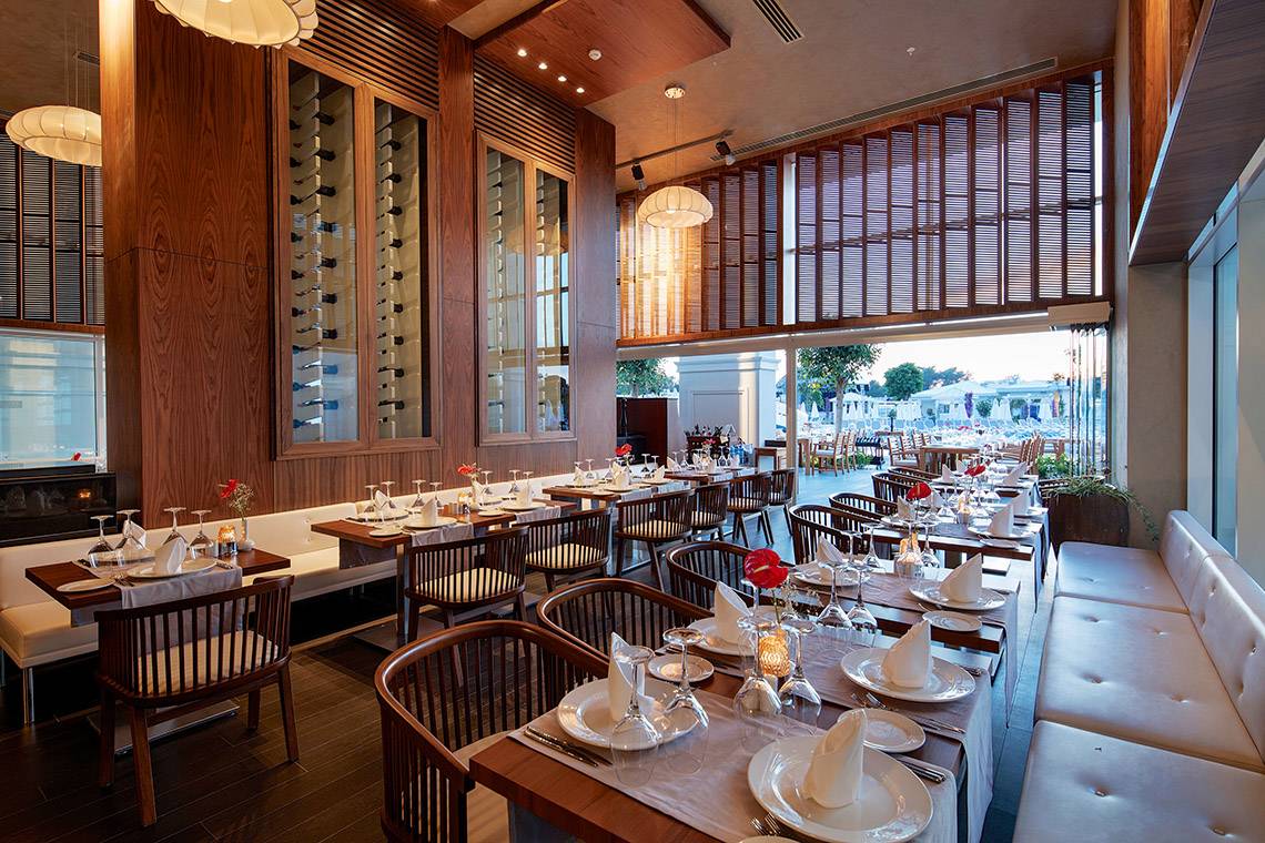 Innenansicht des Restaurants im Titanic Deluxe Golf Belek Hotel mit gedeckten Tischen und Stühlen.