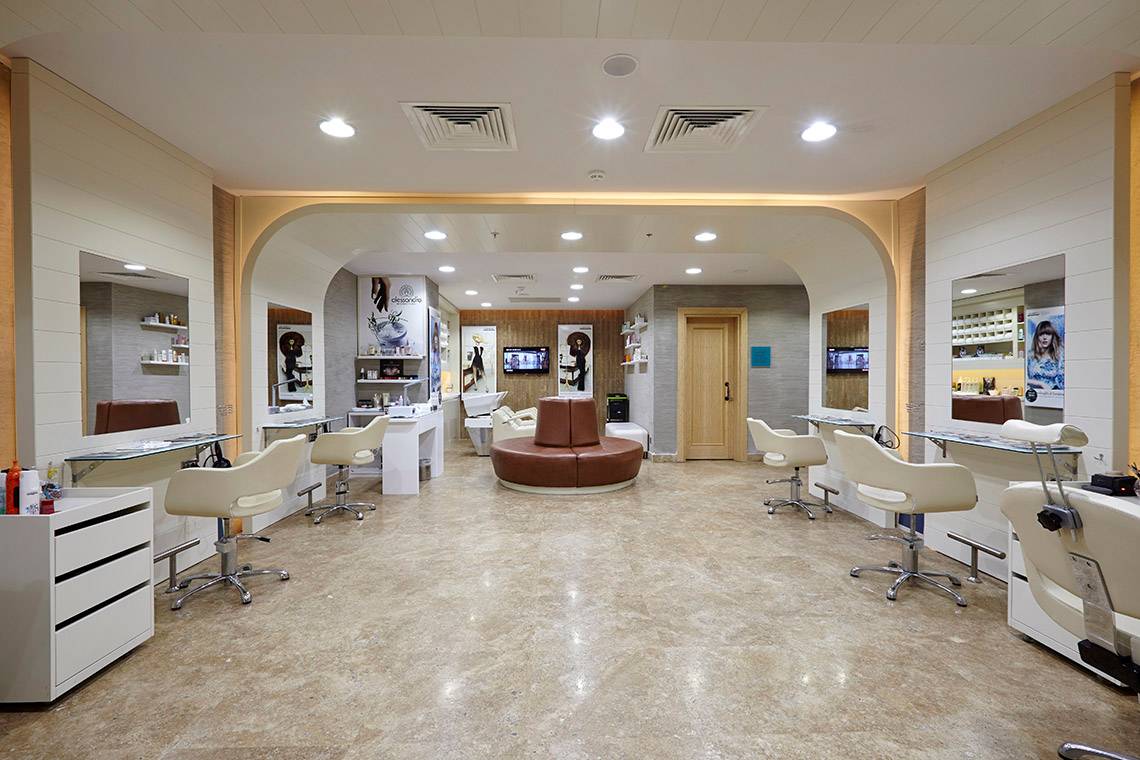 Innenansicht eines Friseursalons mit Stühlen, Spiegeln und Fernsehgeräten.