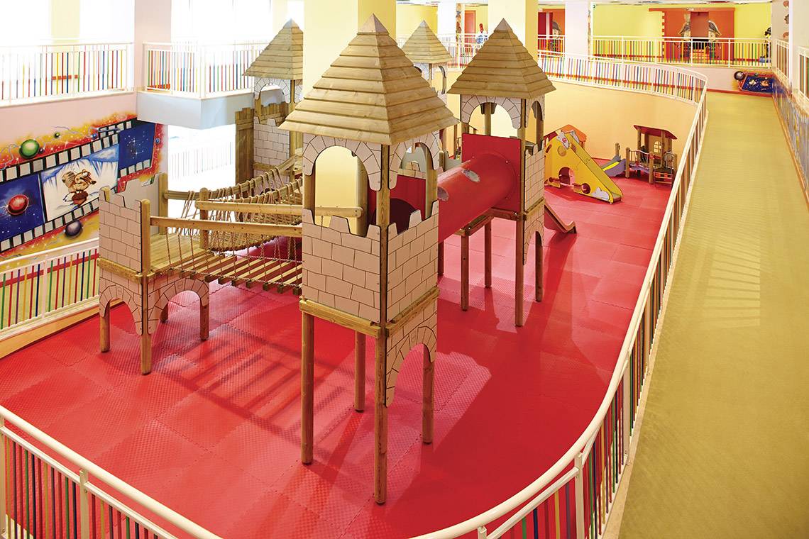 Kinderspielplatz im Titanic Deluxe Golf Belek Hotel mit bunten Holzburgen und roter Spielfläche.