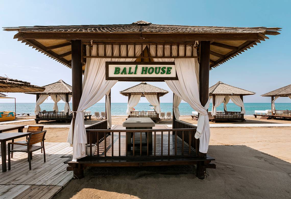 Bali House Strandpavillon mit weißen Vorhängen und Blick auf das Meer.