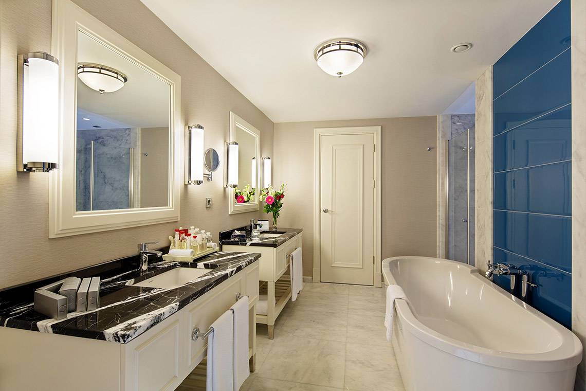 Das Badezimmer im Titanic Deluxe Golf Belek zeigt eine elegante Gestaltung mit zwei Waschtischen, einer Badewanne und blauen Fliesen.