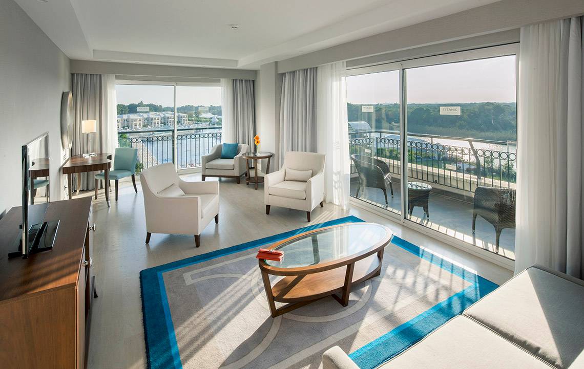 Innenansicht der Suite im Titanic Deluxe Golf Belek Hotel mit Blick auf den Balkon und Fluss.