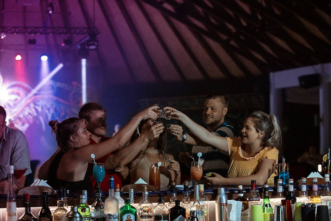 Familie und Freunde stoßen mit Cocktails an der Bar des Bandos Maldives Hotels an