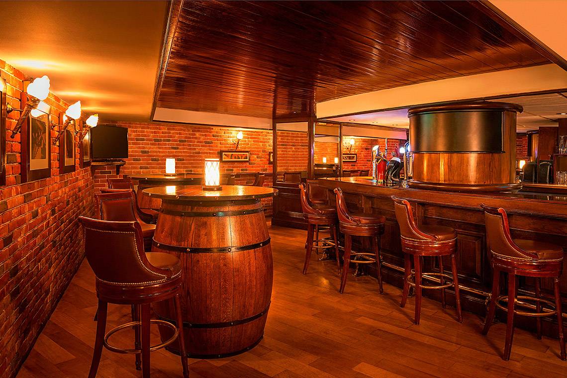 Innenansicht der Bar im Sheraton Abu Dhabi Hotel & Resort mit Holzfass, Barhockern und Holzboden.