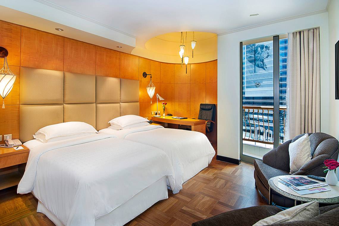 Schlafzimmer im Sheraton Abu Dhabi Hotel & Resort mit zwei Betten, Schreibtisch und Aussicht auf die Stadt.