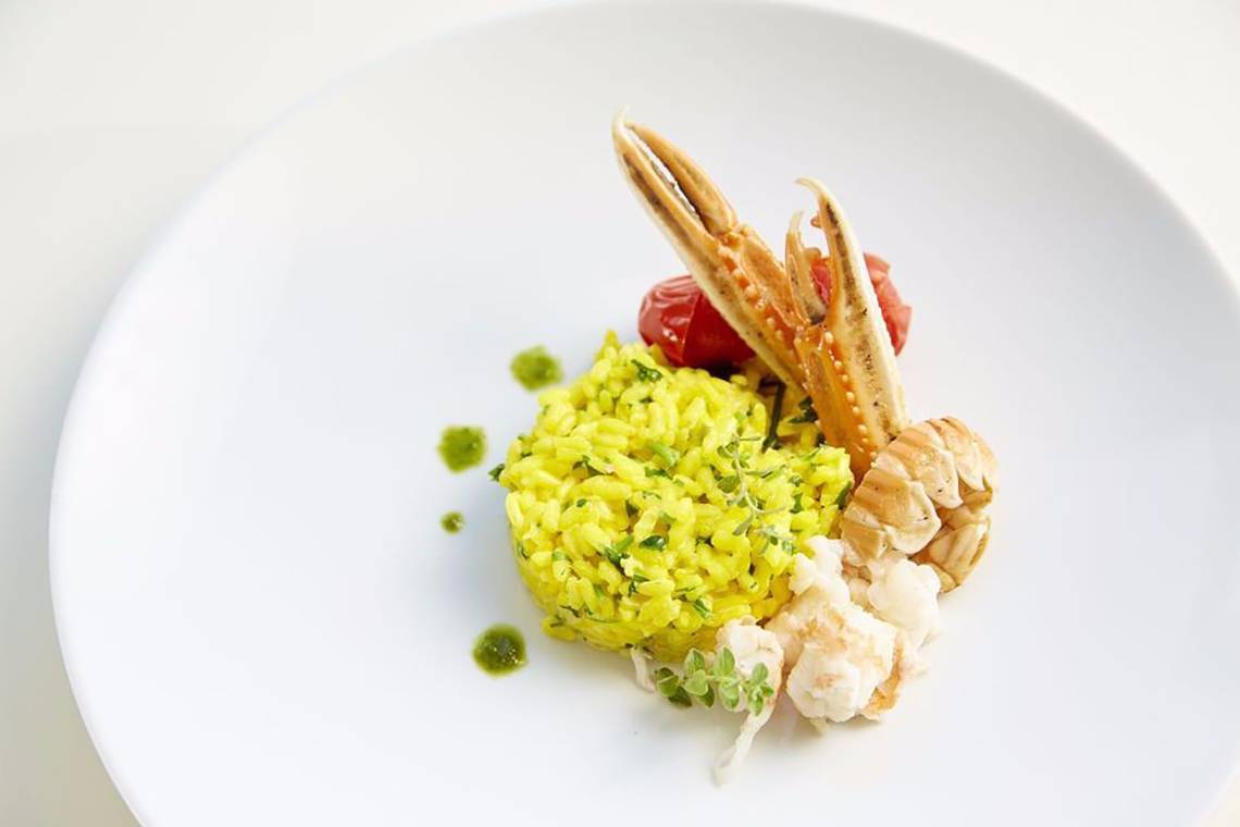 Gebratenes Hummer-Risotto auf einem weißen Teller mit Garnelen und Tomaten.