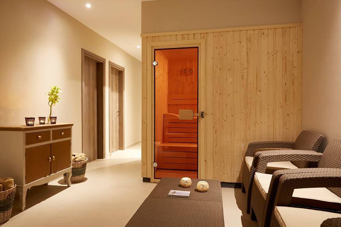 Sauna-Raum im Capo Di Corfu Hotel mit Holzwänden, offener Saunatür und Holzstühlen.