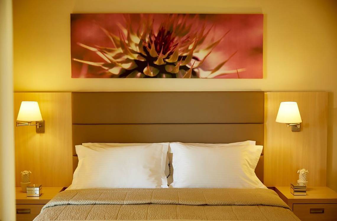 Schlafzimmer im Capo Di Corfu Hotel mit Doppelbett, Nachttischen und Wandkunst.