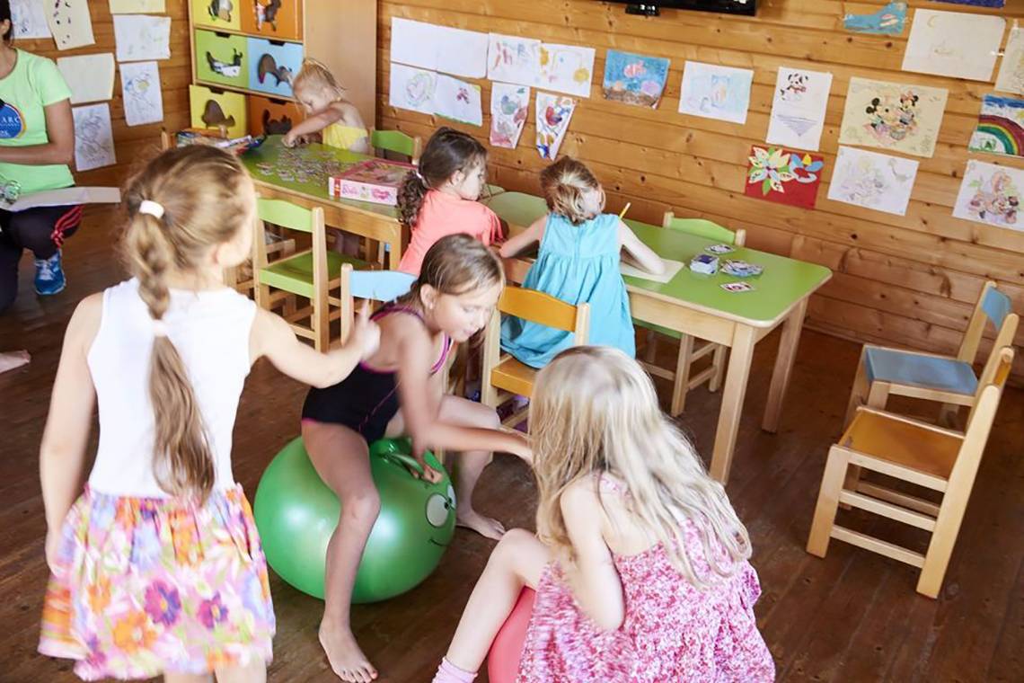 Kleine Mädchen spielen in einem Klassenzimmer mit einem großen grünen Ball.