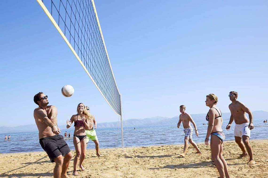 Mehrere Personen spielen Volleyball auf einem Strand am Tag.