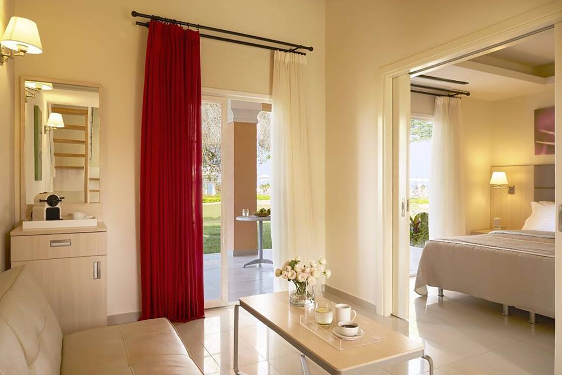 Innenansicht eines Zimmers im Capo Di Corfu Hotel mit offenem Fenster und Blick auf den Garten.