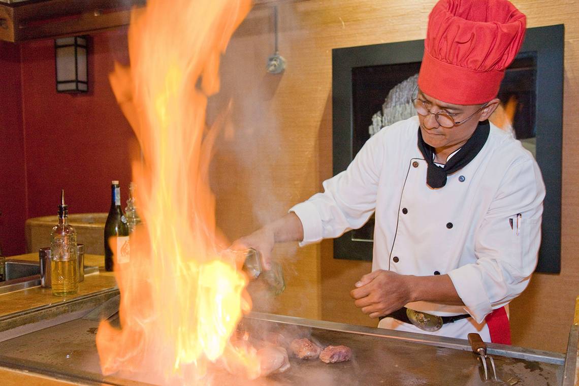 Koch im Restaurant brät Fleisch auf einem Grill mit Flammen.