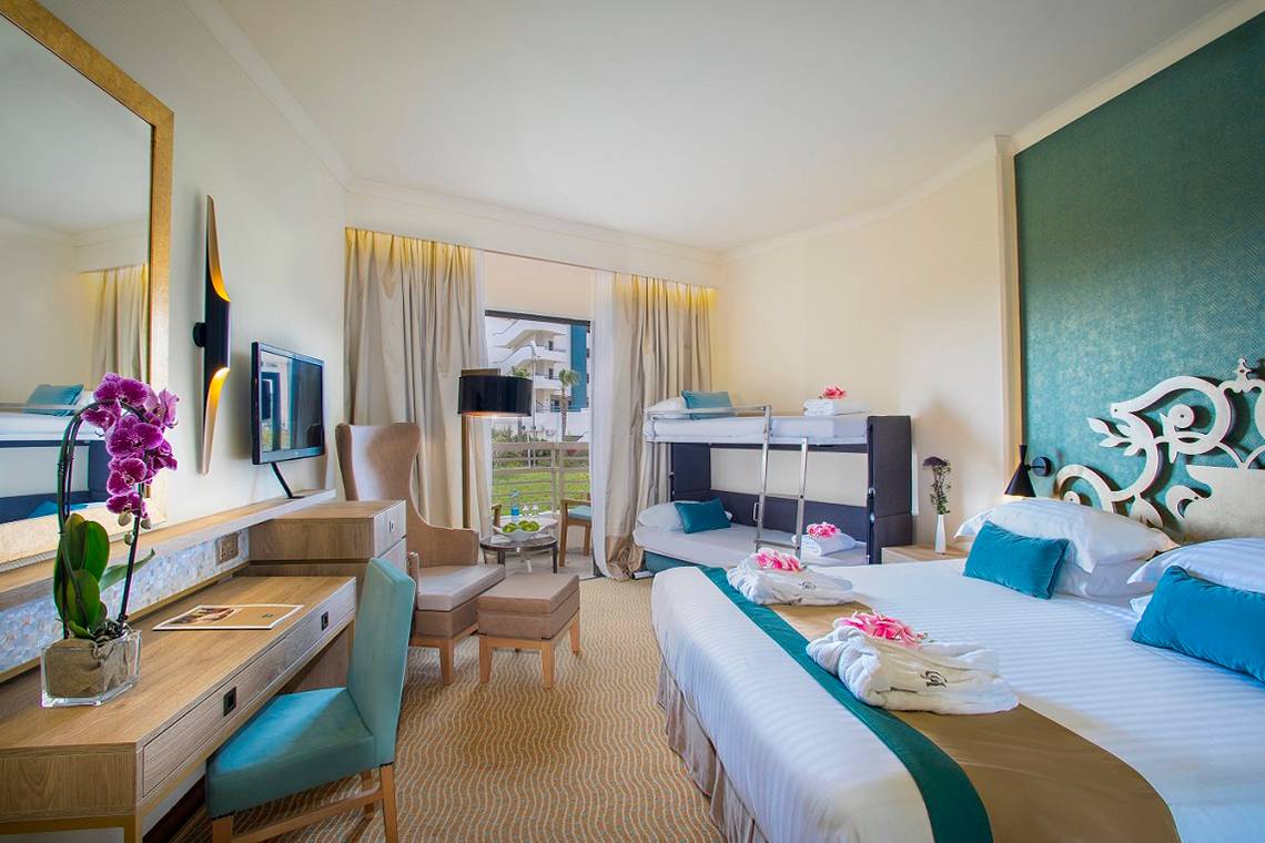 Ein elegantes Hotelzimmer im GrandResort Limassol mit zwei Betten, einem Schreibtisch und einem Spiegel.