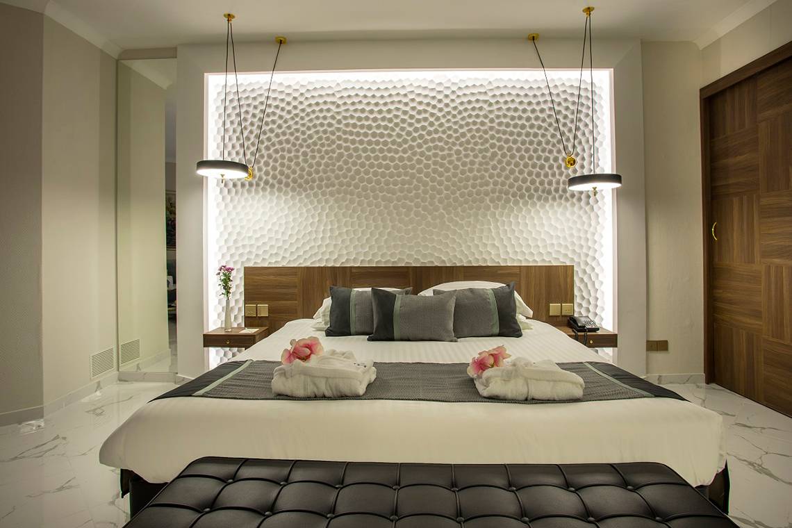 Schlafzimmer im GrandResort Limassol mit zeitgenössischem Design, einem Bett mit weißen und grauen Laken und zwei rosa Rosen auf der Decke.
