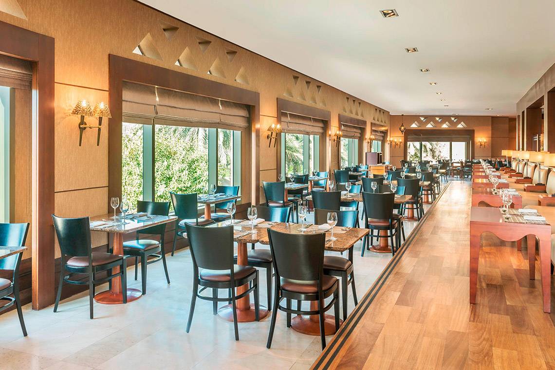 Restaurant im Sheraton Abu Dhabi Hotel & Resort mit vielen Tischen und Stühlen, großen Fenstern und Holzboden.