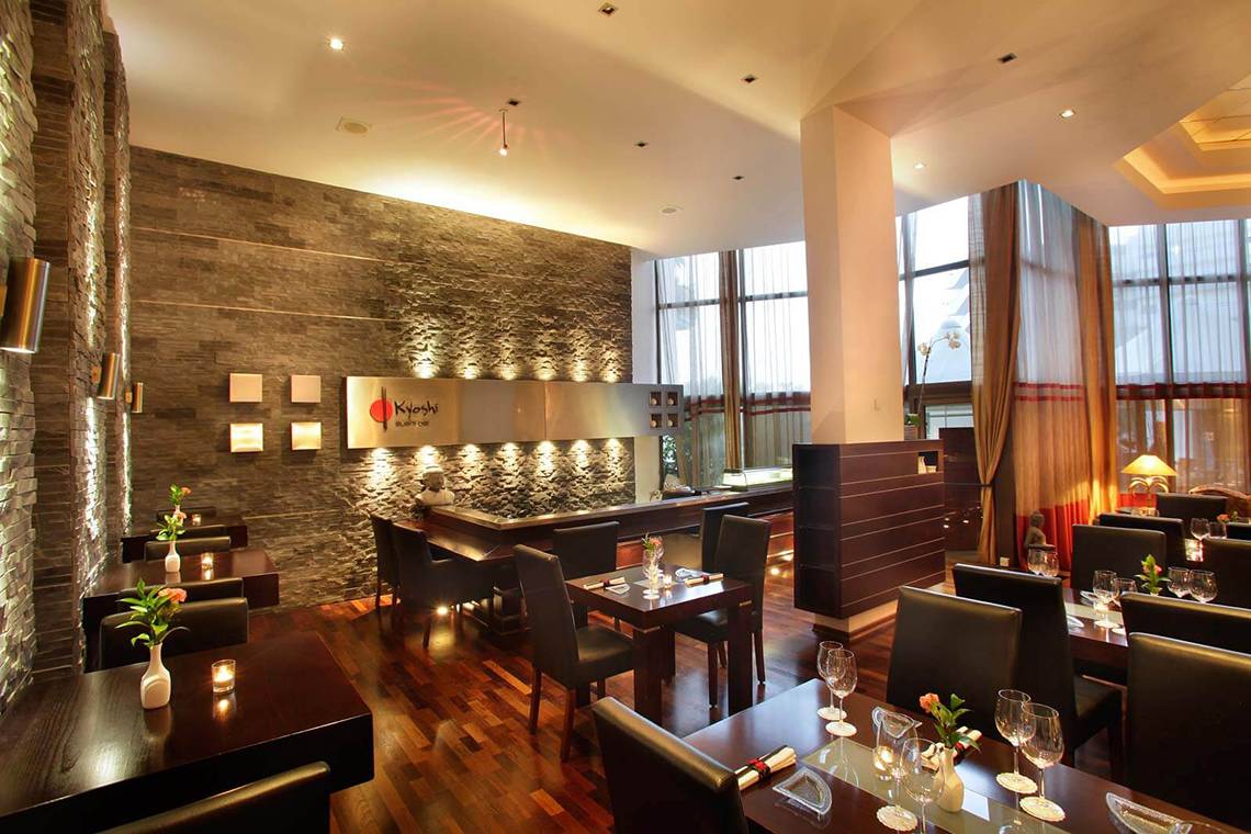 Innenansicht des GrandResort Limassol Restaurants mit Holzböden, Steinwänden und gedeckten Tischen.