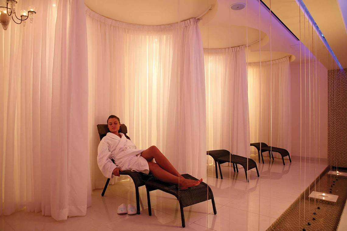 Eine Frau sitzt in einem weißen Bademantel in einem Lounge-Sessel im Wellnessbereich des GrandResort Limassol.