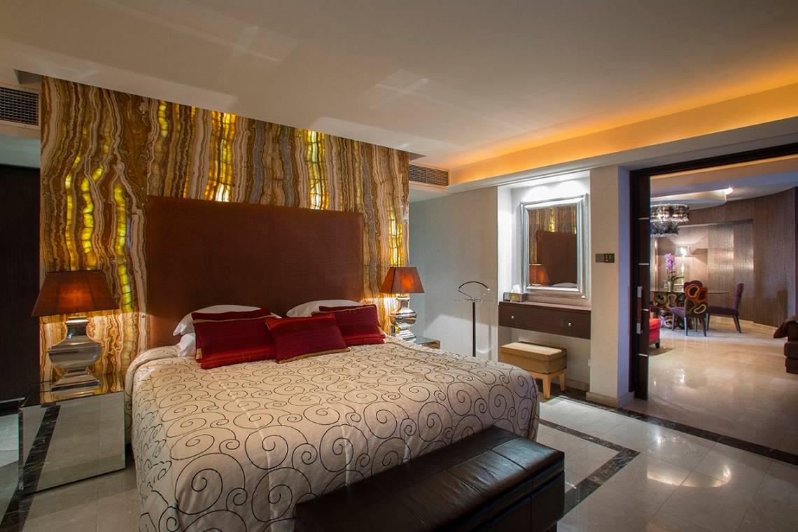 Hotelzimmer im GrandResort Limassol mit luxuriösem Bett, Marmorwand und offenem Eingang.