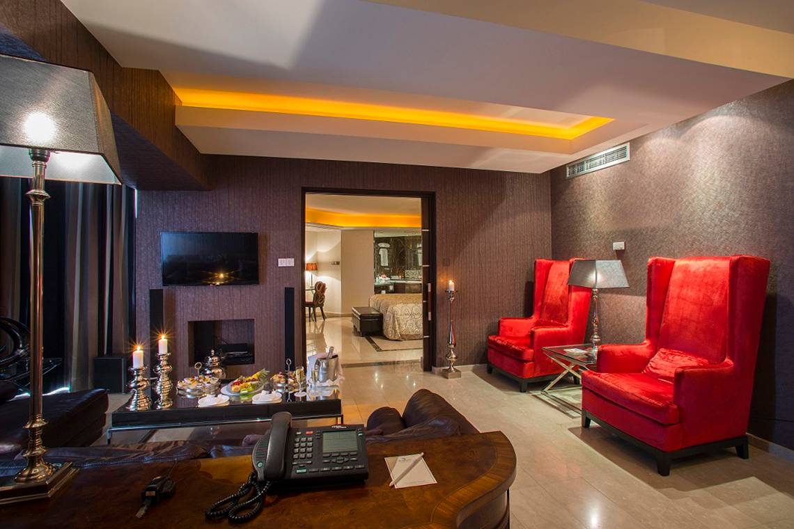 Innenansicht der Suite im GrandResort Limassol mit zwei roten Sesseln, Tisch, Telefon und Kerzen.