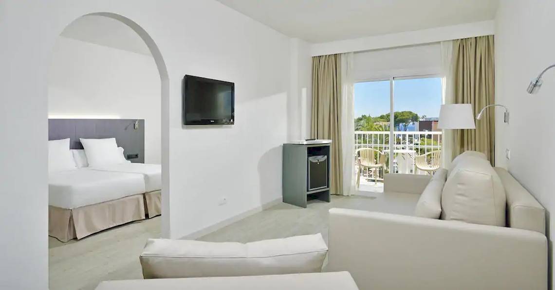 Ein modernes Hotelzimmer mit zwei Betten, einem Fernseher, einem Sofa und einer Terrasse.