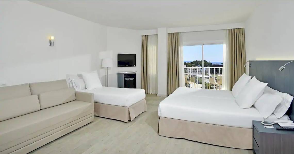 Ein modernes Hotelzimmer mit zwei Betten, einer Couch, einem Fernseher und einer Terrasse mit Blick auf das Meer.