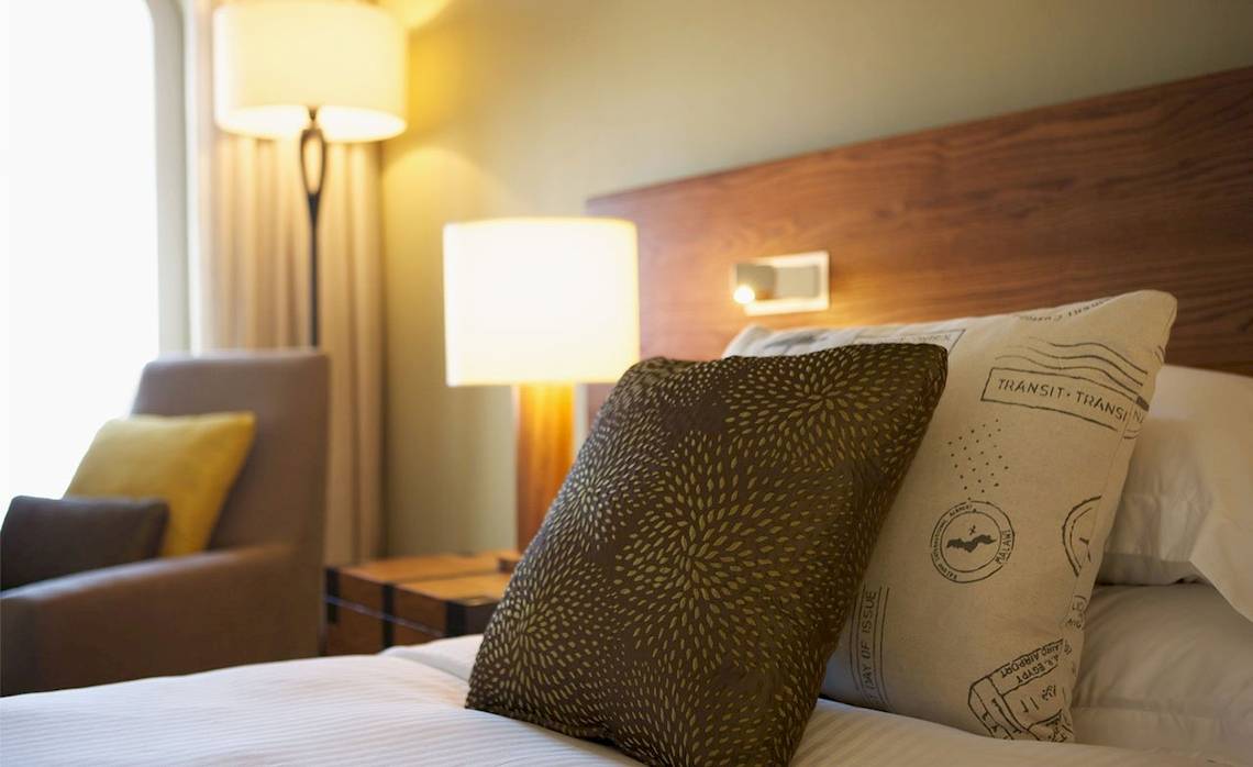 Bett im Outrigger Mauritius Beach Resort mit Kissen und Lampen neben einem Fenster.