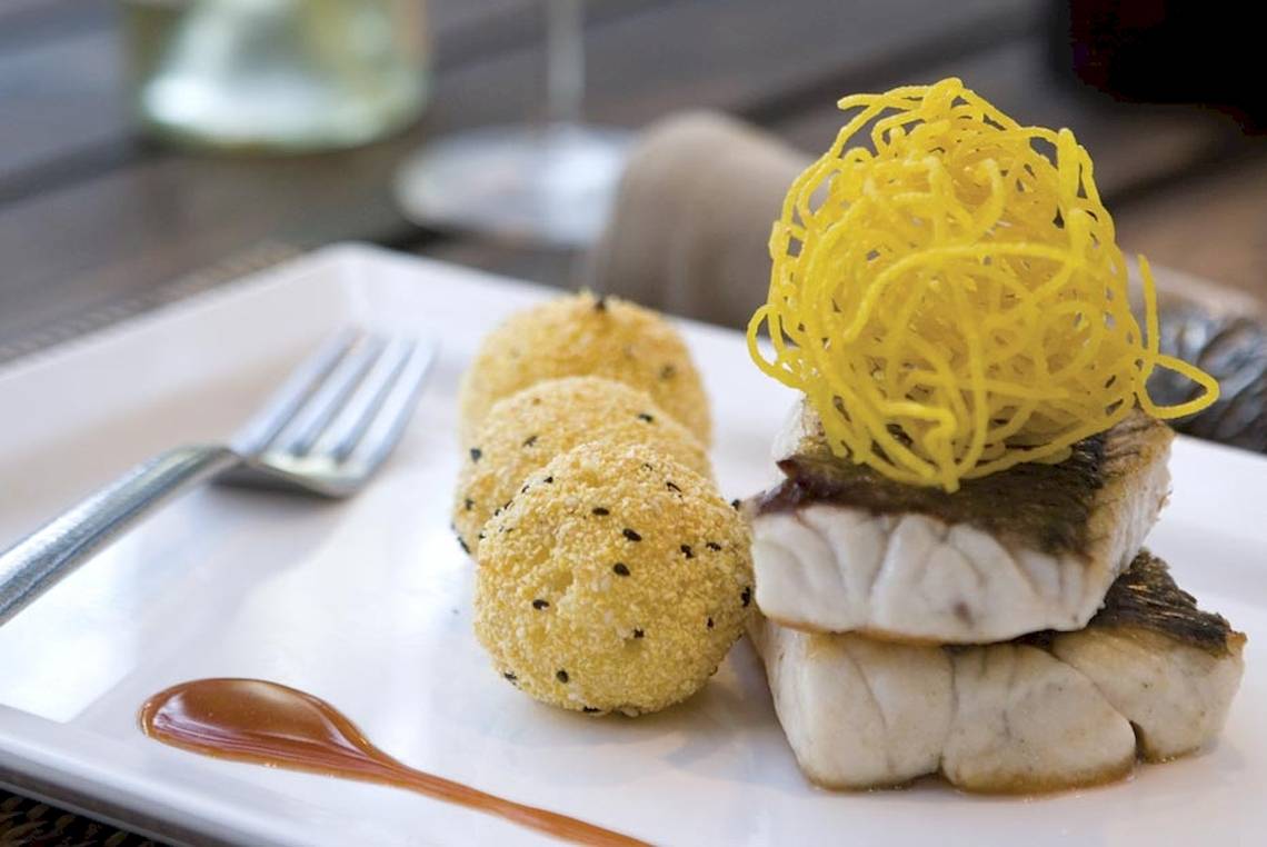 Fischgericht mit frittierten Kugeln und gelber Dekoration auf einem weißen Teller.