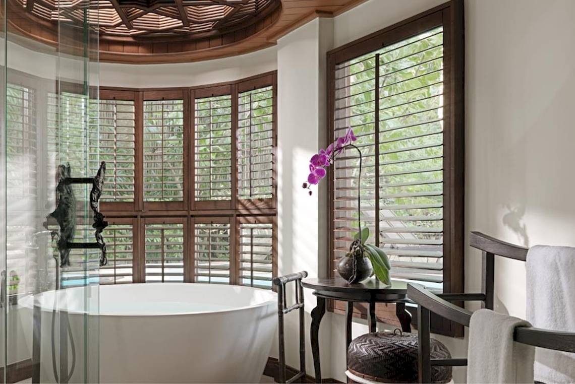 Badezimmer im Rayavadee Hotel mit Badewanne, Holzfenstern und einem Blumentopf auf einem Tisch.
