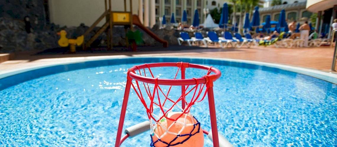 Schwimmbad im Princess Inspire Tenerife Hotel mit einem roten Basketballkorb und einer Rutsche im Hintergrund.