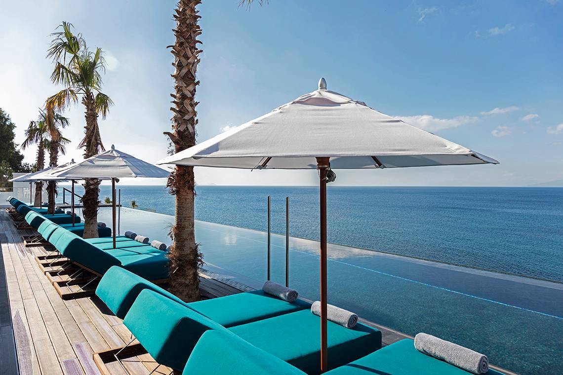 Außenterrasse des Mitsis Summer Palace Beach Hotels mit Liegen und Sonnenschirmen, die zum Meer zeigen.