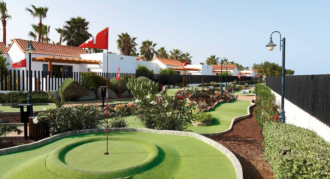 Minigolfkurs vor dem Hotel Barcelo Fuerteventura Castillo mit roten Flaggen und Palmen im Hintergrund.