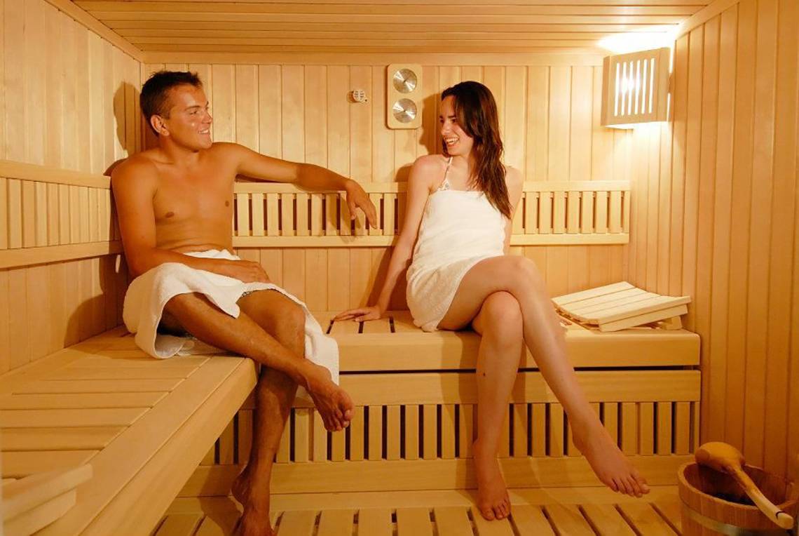 Ein Paar genießt Zeit in der Sauna des Platanista Hotels, beide tragen Handtücher.