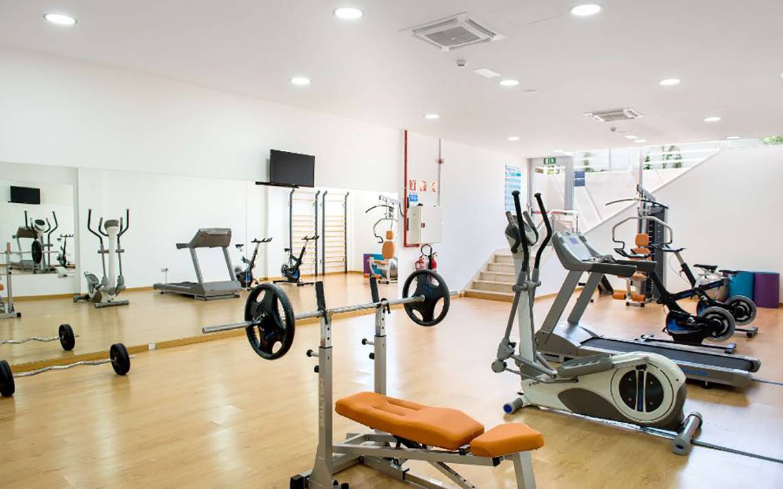 Fitnessraum im Alexandre Hotel Troya mit diversen Trainingsgeräten und Spiegeln.