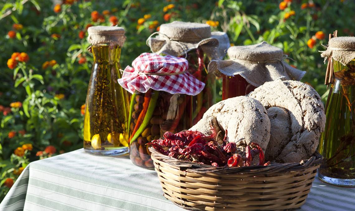 Ein Korb mit Brot und Gewürzen auf einem Tisch mit eingelegten Gemüsen und Öl.