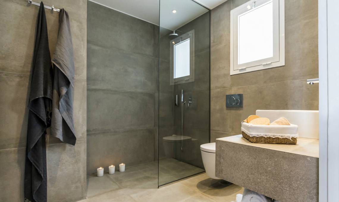 Badezimmer im Candia Park Village Hotel mit grauen Fliesen, Glasdusche und Waschbecken.