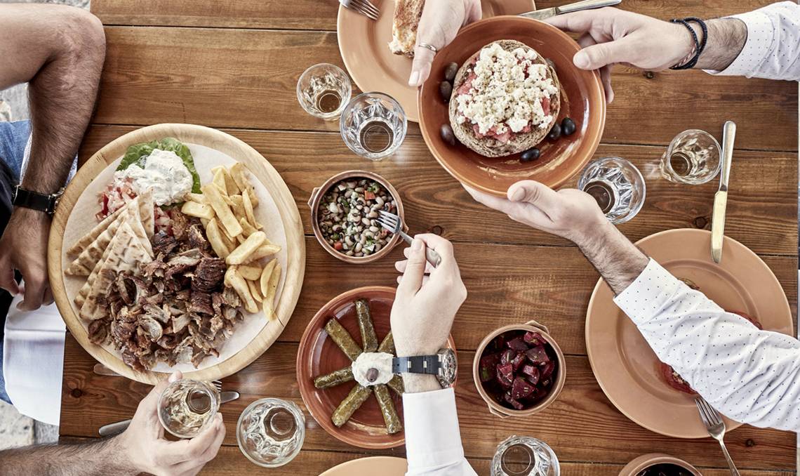 Gruppe isst im Candia Park Village mit verschiedenen Gerichten wie Gyros, Pommes, Hummus und Salat.