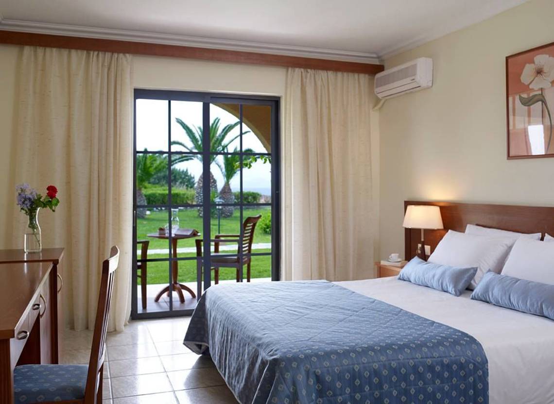 Schlafzimmer im Porto Bello Beach Hotel mit Bett, Tisch und Stuhl vor einer Terrasse