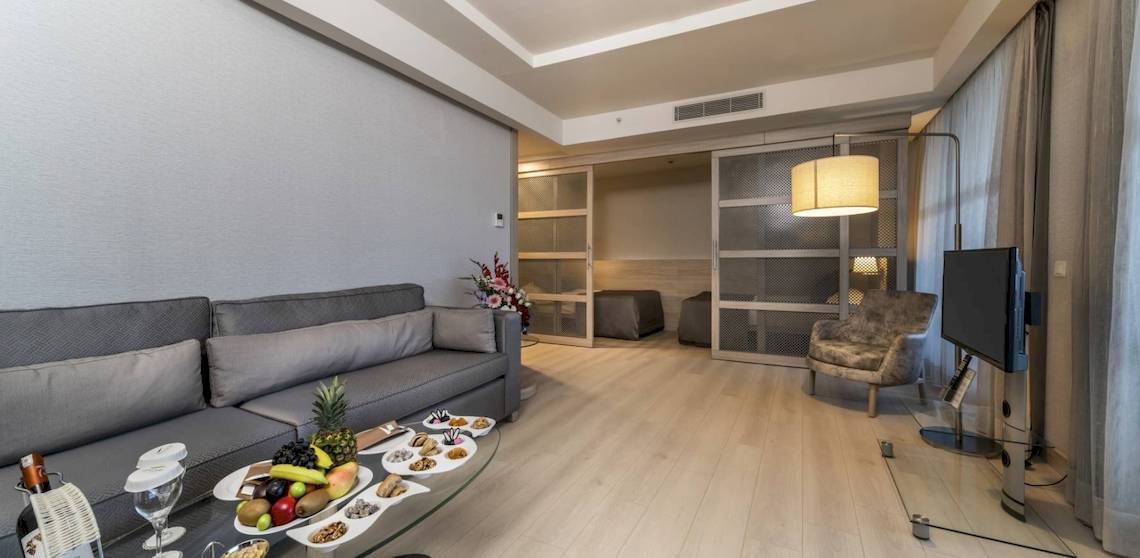 Das Wohnzimmer des Concorde De Luxe Resorts mit grauer Couch, Tisch voller Früchte und Fernseher.