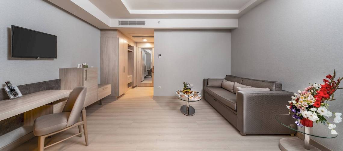 Innenansicht einer Suite im Concorde De Luxe Resort mit Fernseher, Schreibtisch, Stuhl, Sofa und Blumen